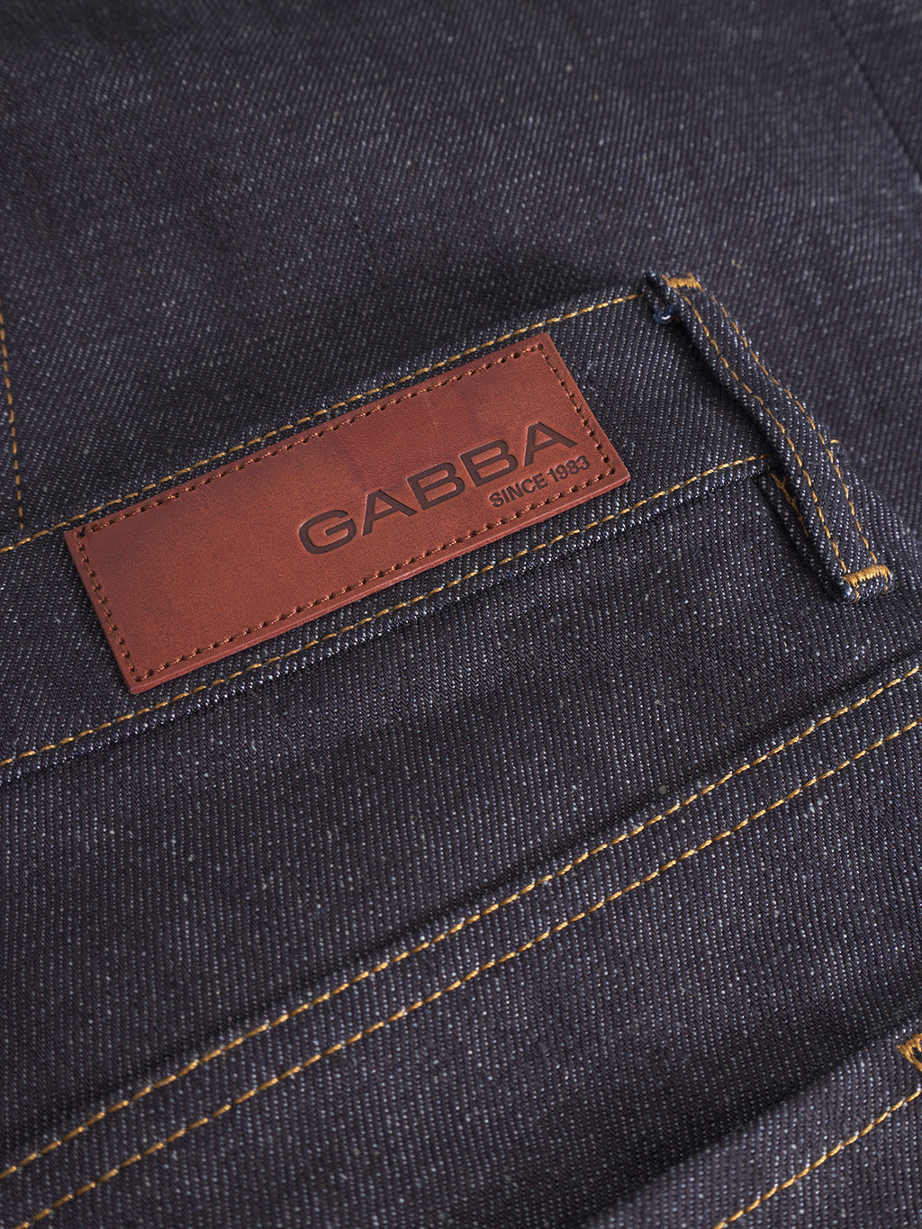 Close-up of Gabba Marc Tana dark blue denim straight-fit jeans with yellow stitching and a brown leather patch above the back pocket embossed with GABBA SINCE 1983.