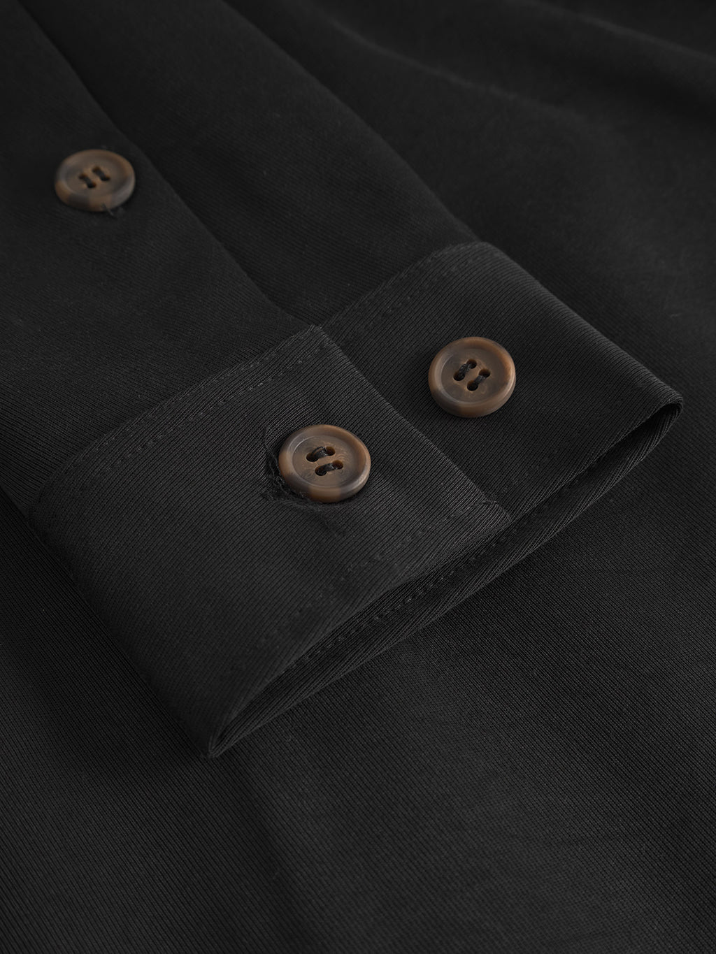 Close-up of the cuff on the Gabba Jens Over Lupo LS - Black: an oversized shirt with brown buttons. The smooth, subtly textured fabric is ideal for everyday layering, and the buttons are securely sewn on both cuff and placket.