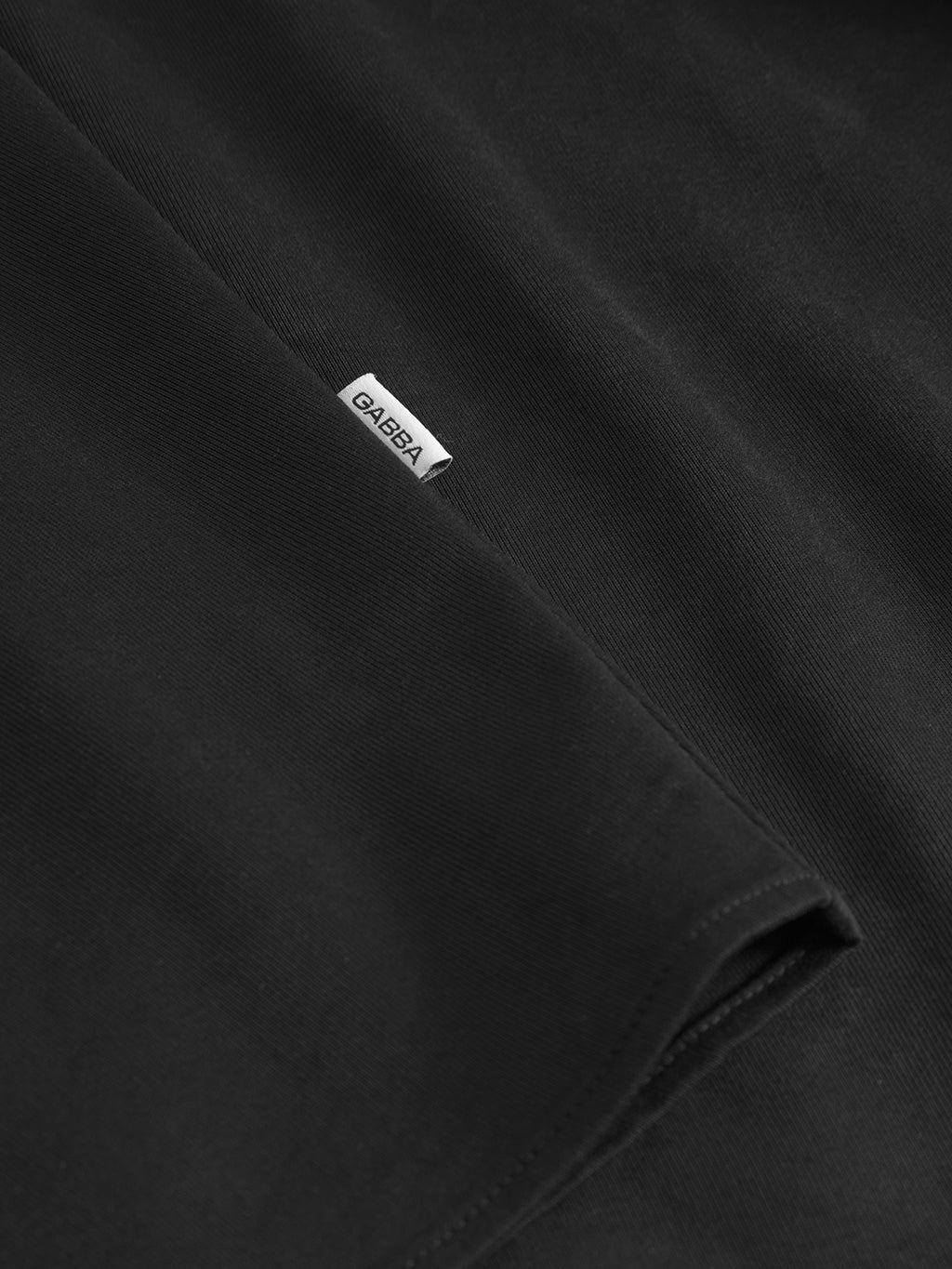 Close-up of the black Jens Over Lupo LS by Gabba, featuring a small white Gabba label on the seam. The smooth, neatly folded fabric gives a modern drape, ideal for an oversized shirt with a relaxed and elevated style.
