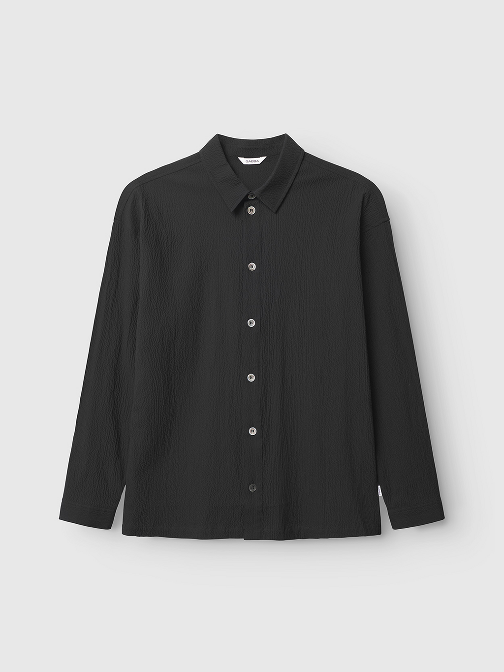 The Gabba Jens Over Siro LS GOTS - Black is a long-sleeve seersucker shirt featuring textured fabric, a classic collar, and white buttons, shown on a plain white background.