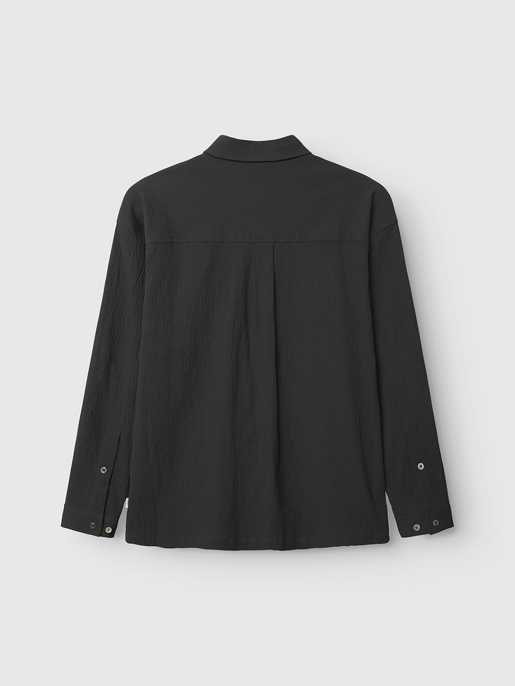 Back view of the Gabba Jens Over Siro LS GOTS - Black shirt, featuring textured, wrinkle-free seersucker fabric, buttoned cuffs, and a simple collar, shown against a plain light gray background.