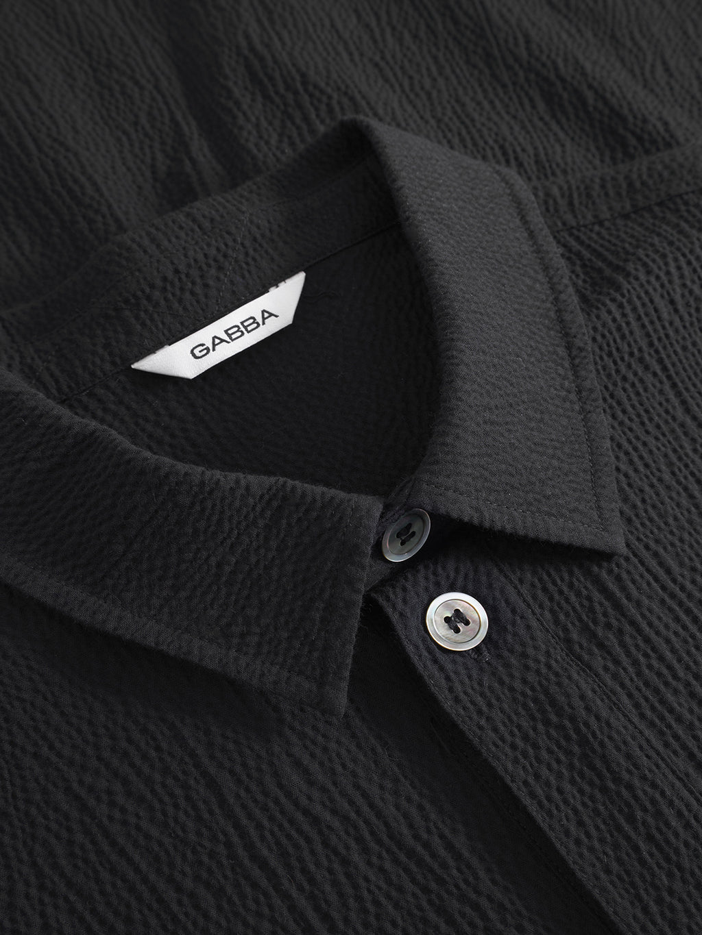 Close-up of the Gabba Jens Over Siro LS GOTS - Black shirt with a textured, wrinkle-free finish, pointed collar, two visible buttons, and a white Gabba label inside the collar.