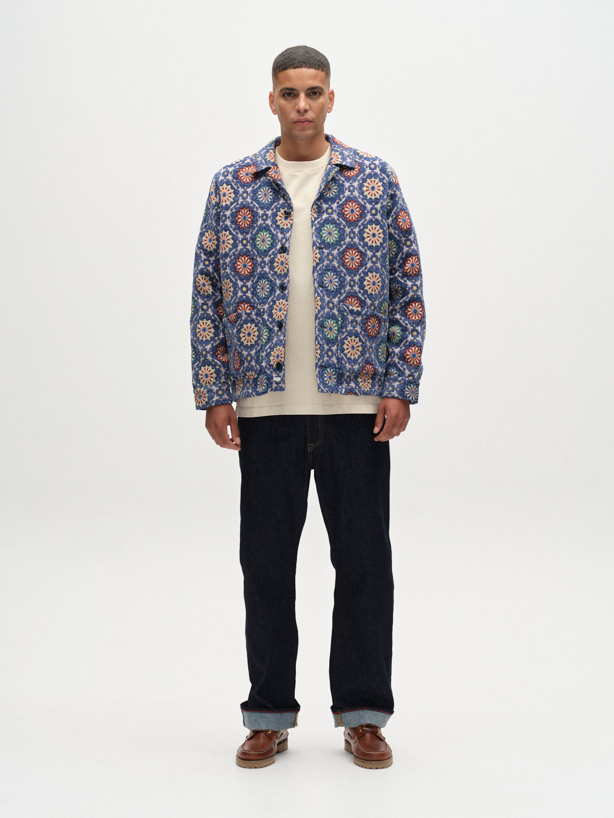 A man faces forward against a plain white background, wearing the Gabba GABsimone Nava LS - Multi Pattern overshirt with a white shirt, dark jeans, and brown shoes.