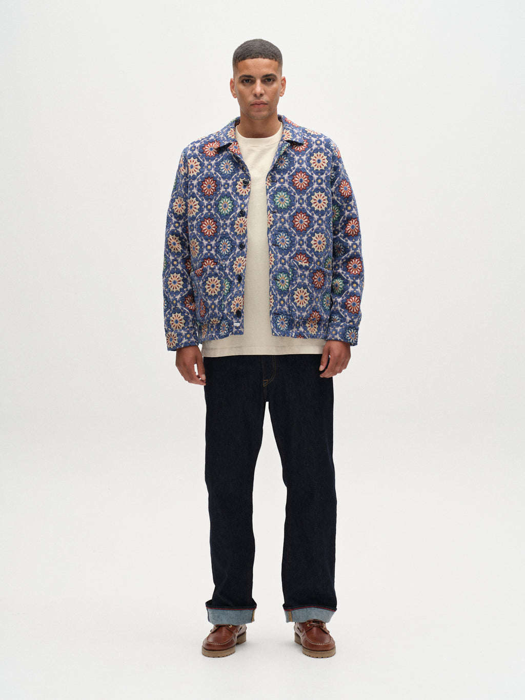 A man stands against a white background, wearing the Gabba Simone Nava LS - Multi Pattern jacket over a beige shirt, paired with dark jeans and brown shoes. He faces forward with arms relaxed at his sides.