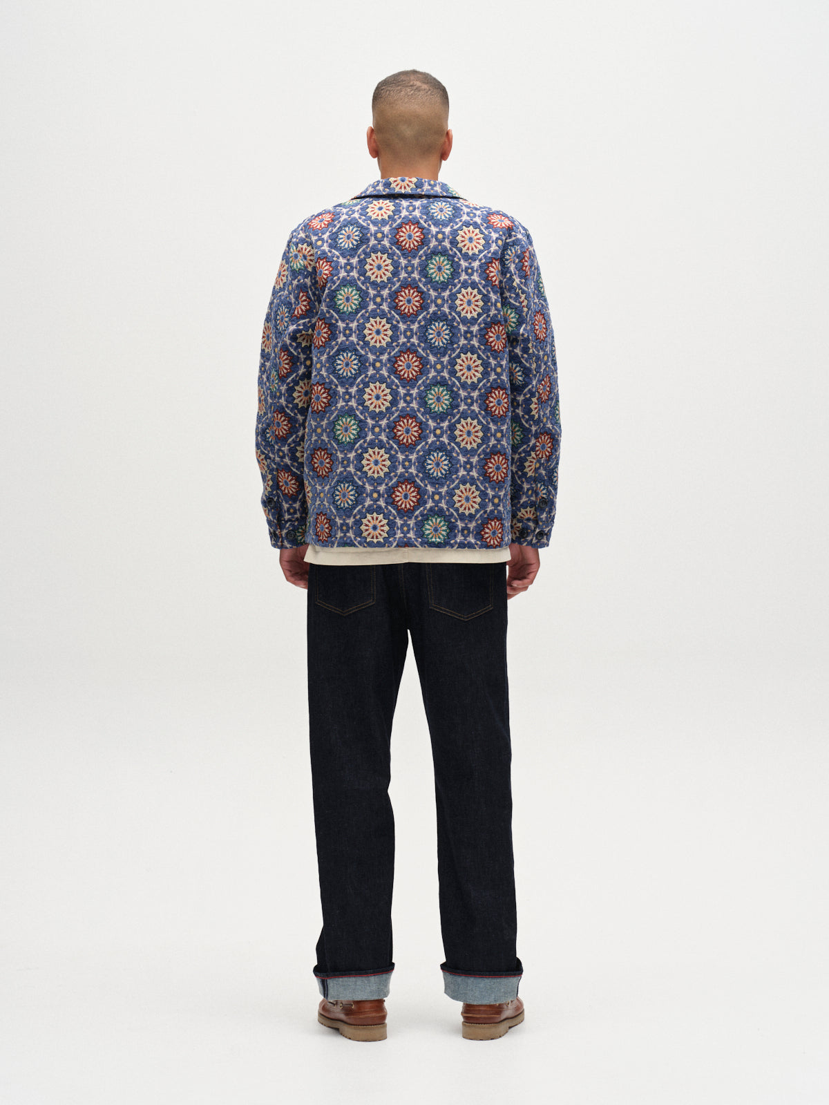 A person stands facing away, wearing the Gabba GABsimone Nava LS - Multi Pattern overshirt, paired with dark jeans and brown shoes against a plain white background.