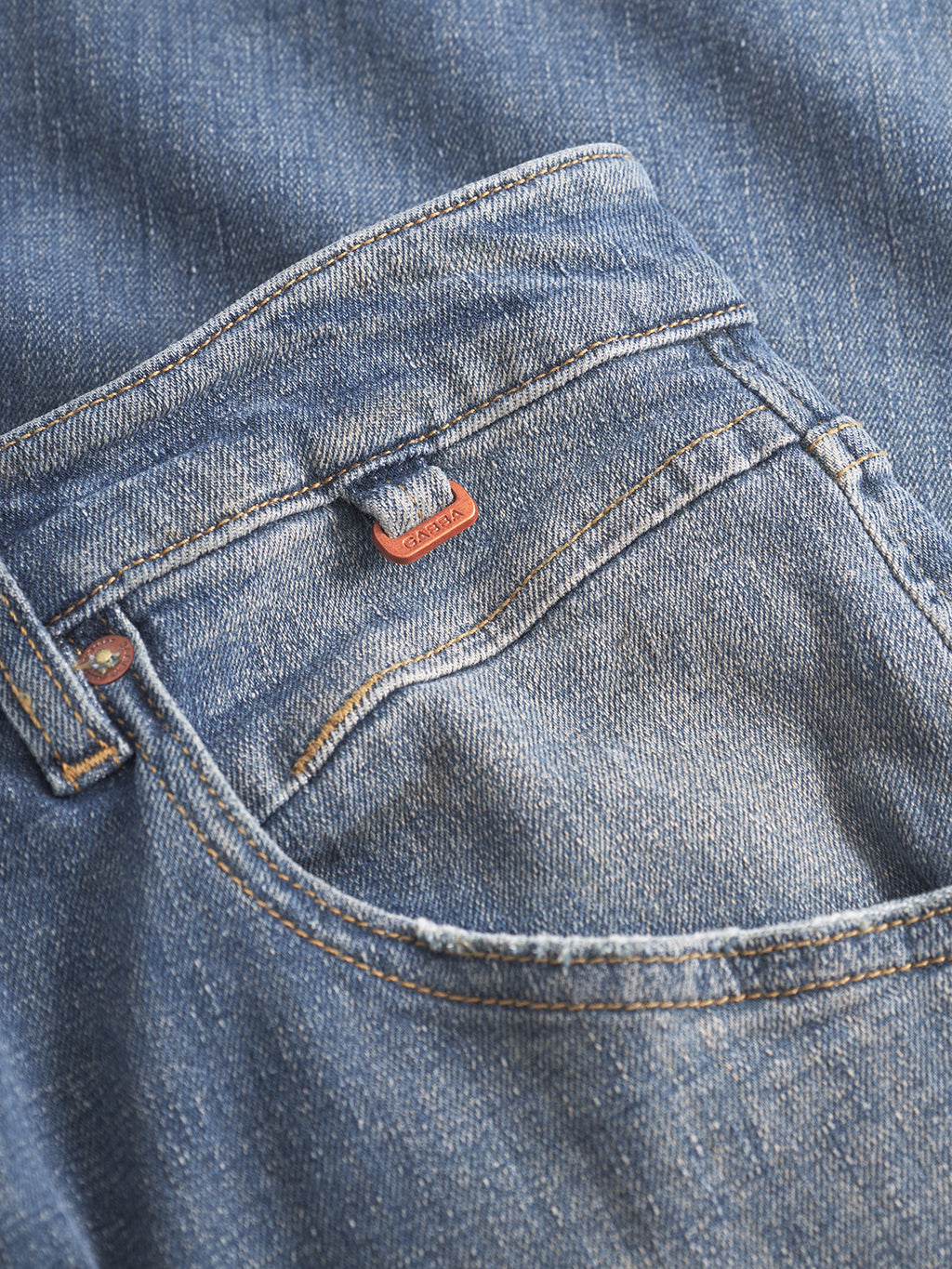 Close-up of Gabba Alex Ulio mid blue denim jeans featuring a relaxed tapered fit, front pocket with orange stitching, and a small orange fabric loop above the pocket for stretch comfort.
