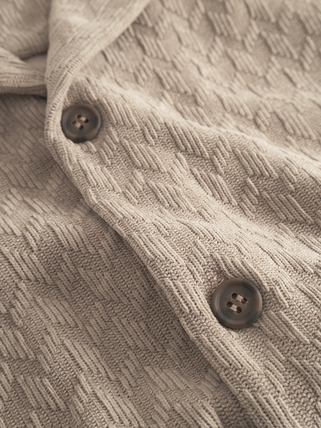 Close-up of the Jens Over Diam SS in Sand by Gabba, featuring beige textured knit fabric with a geometric pattern and two dark brown buttons—perfect for a cozy, neutral overshirt look.