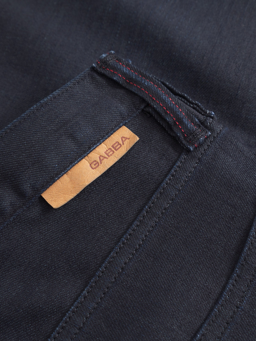 Close-up of Carl Anark Fara dark blue denim by Gabba shows a tan leather brand tag, visible stitching, belt loop, and stretch fabric for comfort and easy movement.