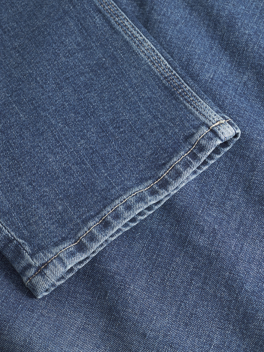 A close-up of the hem and stitching on the Carl Jingo - Dark Blue Denim jeans by Gabba showcases their relaxed silhouette and quality craftsmanship, with one pant leg resting atop another section of denim fabric.
