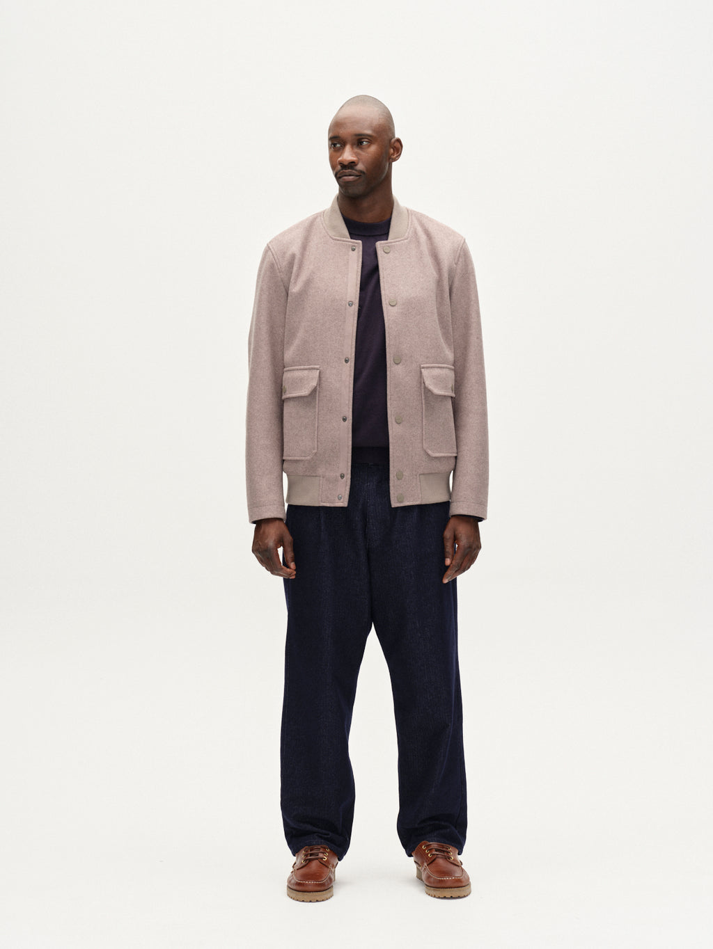 A man faces forward against a white background wearing the Gabba Orta Wox - Sand windproof jacket with front pockets, paired with a dark shirt, loose navy pants, and brown shoes. His expression is neutral and his posture relaxed.