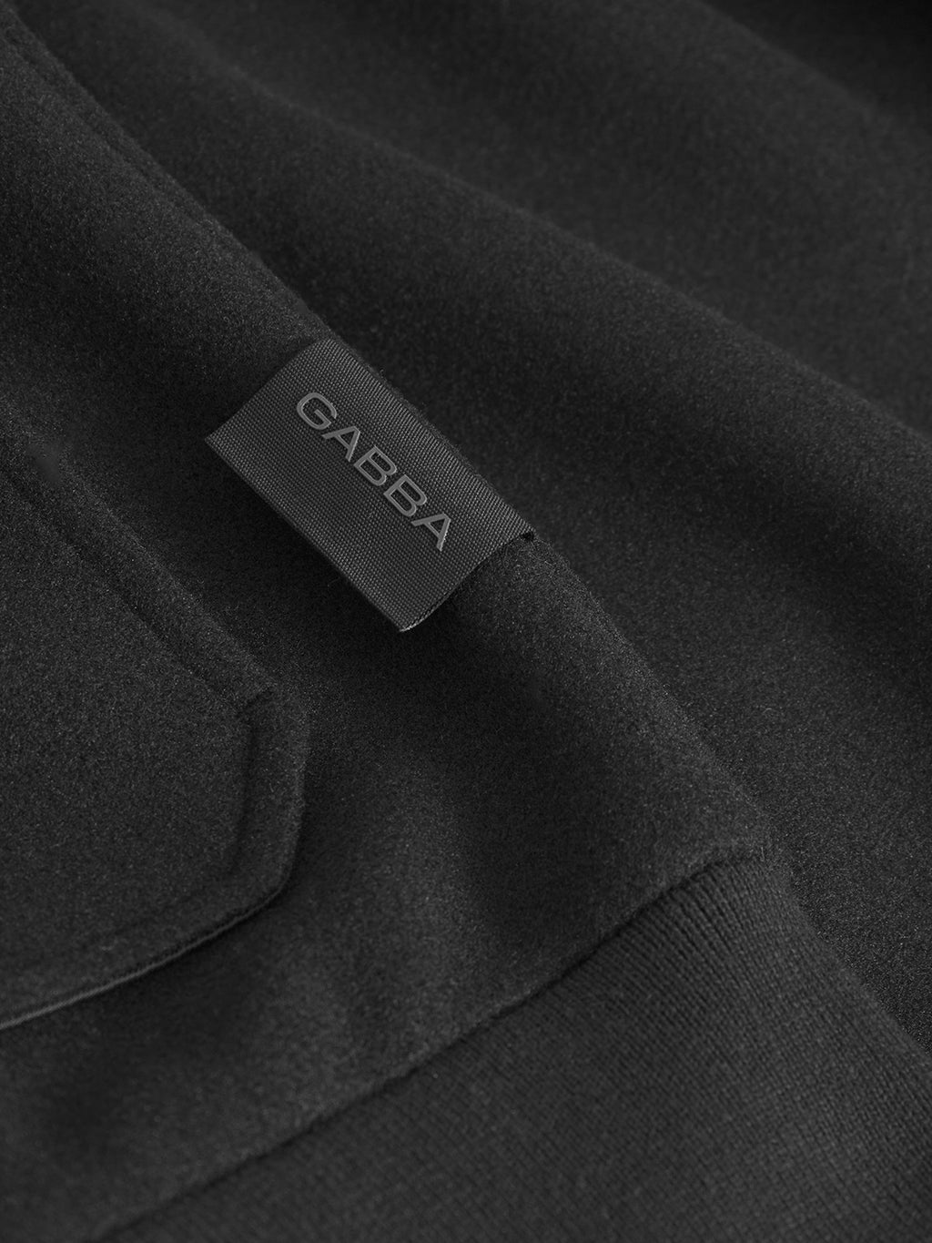 Close-up of the Orta Wox - Black bomber jacket by Gabba, crafted from soft performance fabric. Features a black tag with white Gabba lettering and visible stitching that showcases its quality craftsmanship.