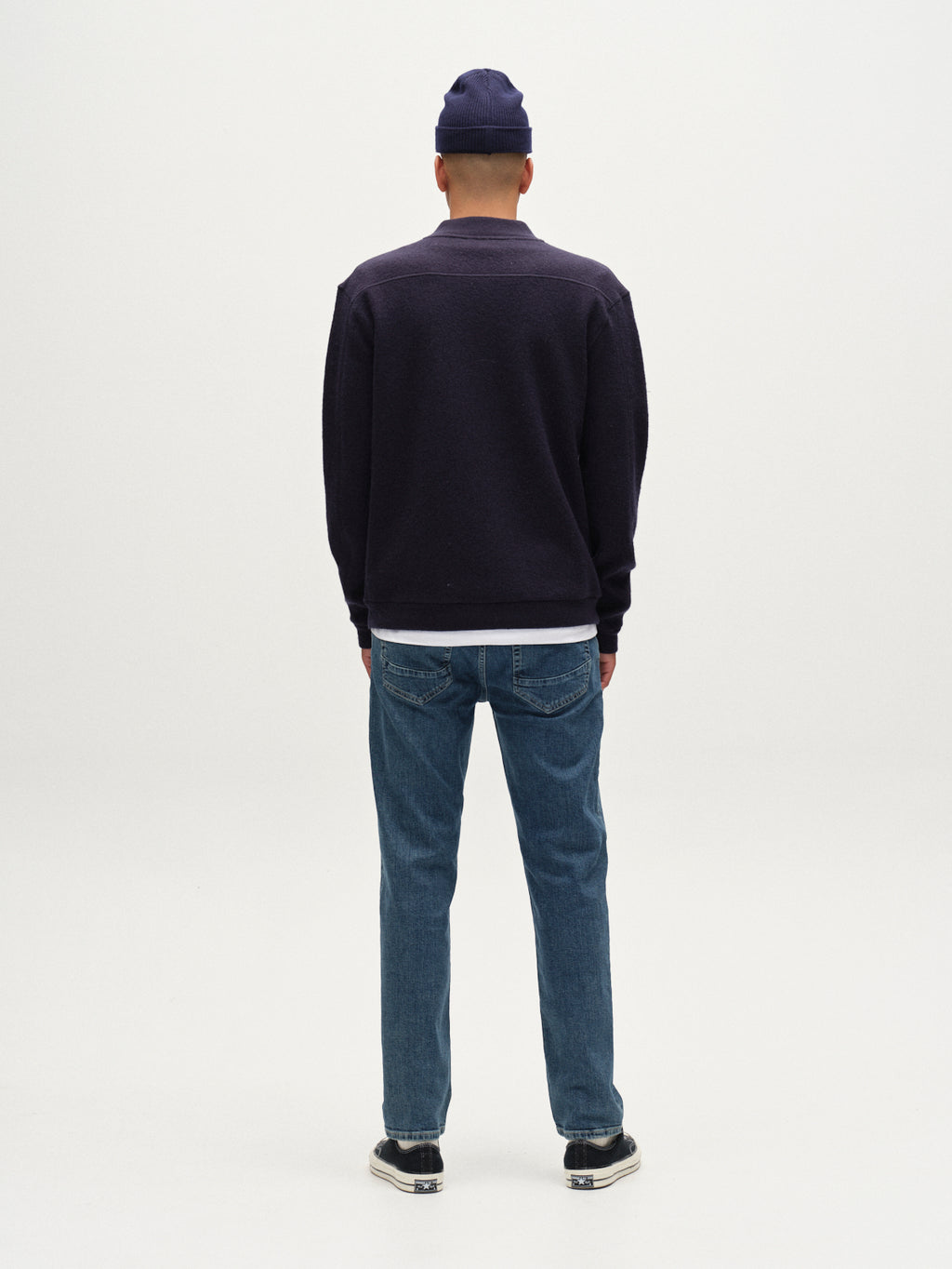 A person wearing a dark beanie, dark jacket, and Gabba Marc Jingo straight-leg jeans in dark blue denim stands facing away from the camera against a plain white background.