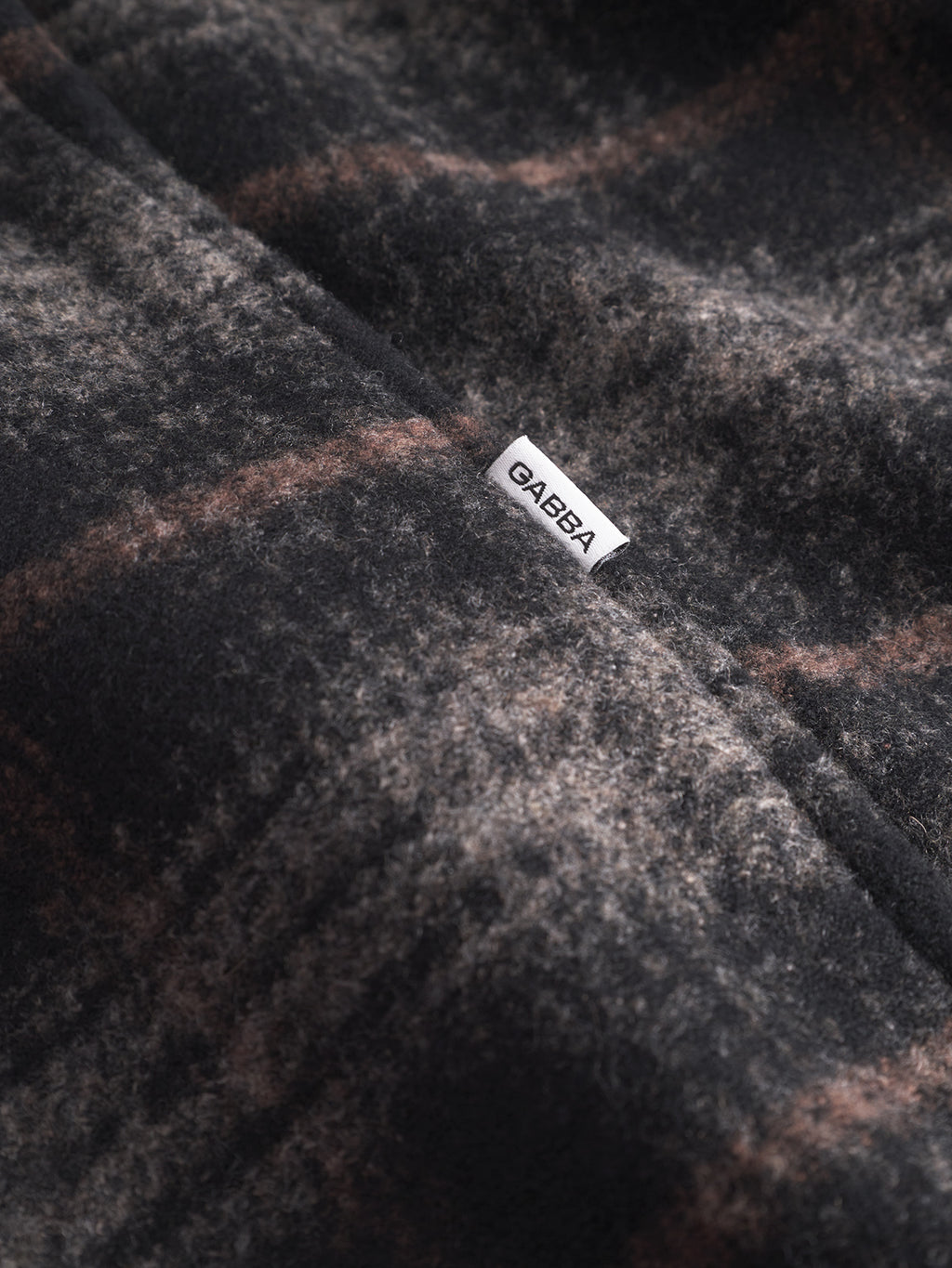 Close-up of the Leeds Cast - Multi Check fabric by Gabba, featuring a textured, brushed wool blend in dark and light brown plaid with a small white Gabba tag—ideal for highlighting its classic winter check pattern.