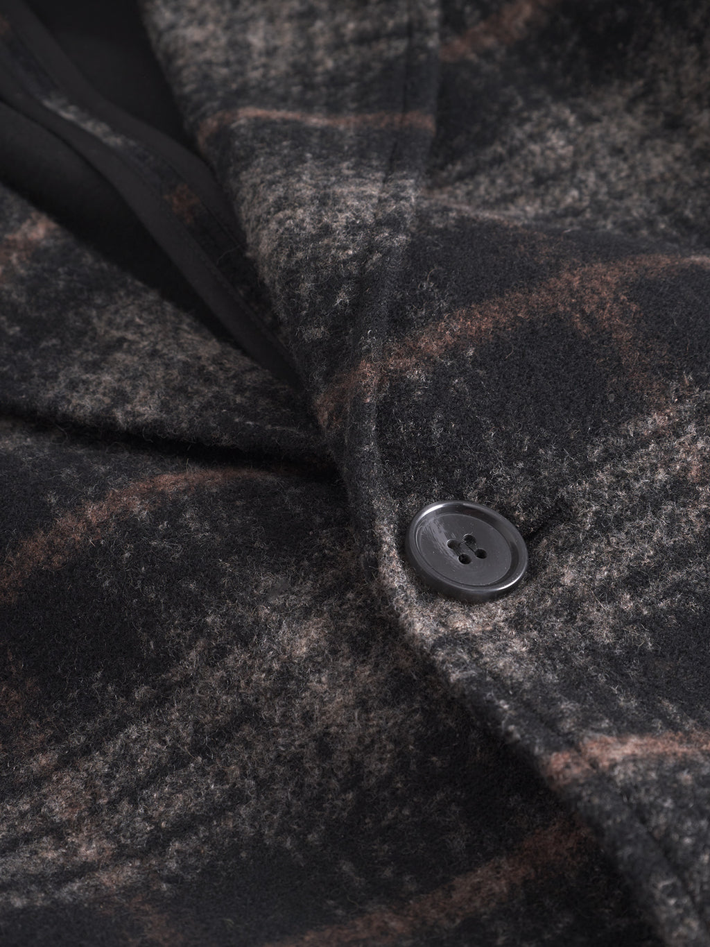 Close-up of the Gabba Leeds Cast - Multi Check coat, showcasing its dark plaid brushed wool-blend fabric with a subtle brown and gray check pattern and a visible black four-hole button.