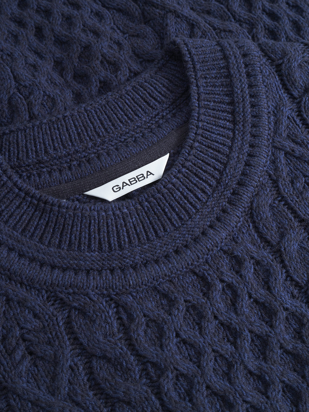Close-up of the Tokyo Cable LS sweater in navy, featuring a standout cable knit design and ribbed collar. A white tag inside the collar displays the Gabba brand name in black letters.