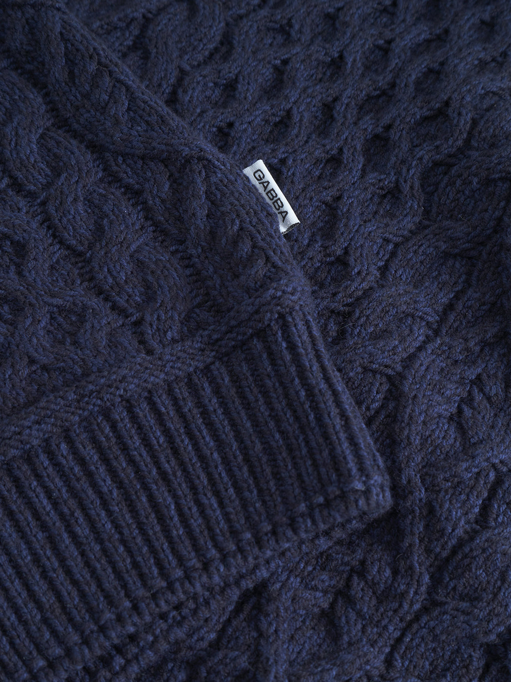 Close-up of the Gabba Tokyo Cable LS in navy, showcasing its classic cable-knit pattern, ribbed cuff, and a small white fabric label sewn into the seam.