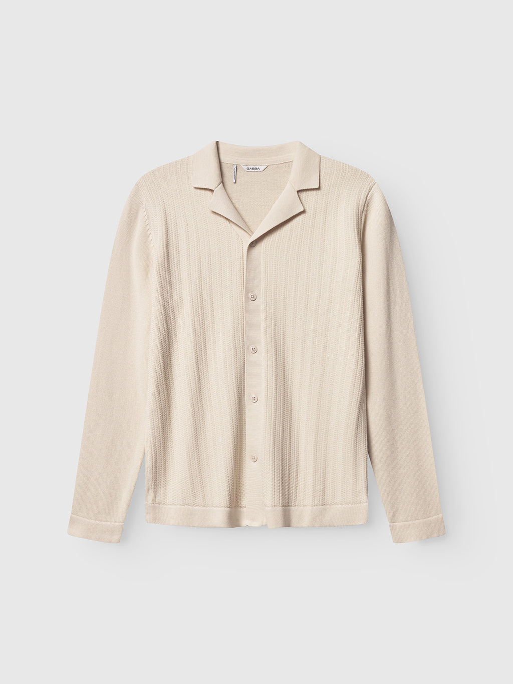 The Gabba Sakai Wong LS - White Almond is a cream-colored, long-sleeve cardigan with a resort collar and button-up front, made from 100% cotton in a modern knit, shown flat on a light gray background.