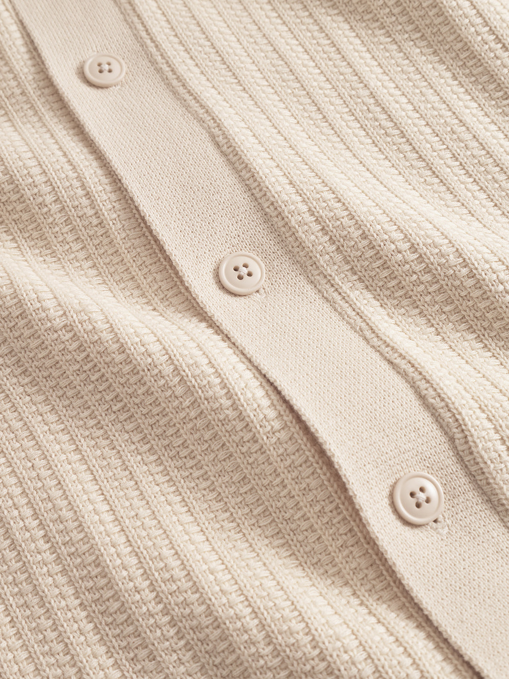 Close-up of the Gabba Sakai Wong LS in White Almond, showing its beige modern knit fabric with ribbed texture and a row of four matching buttons along a vertical seam.