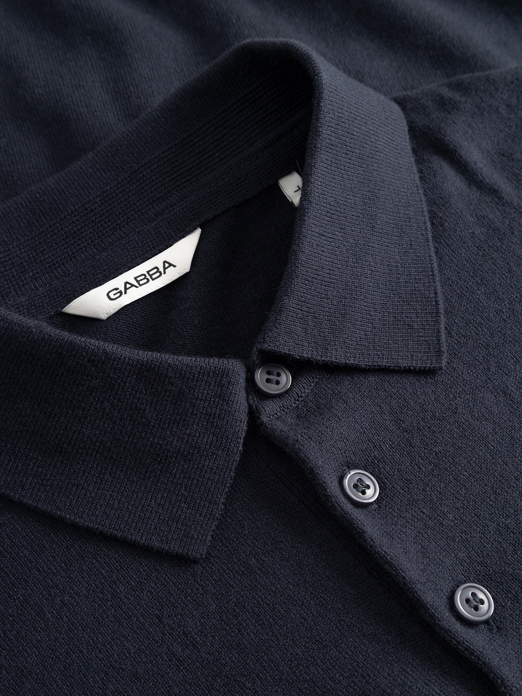 Close-up of the Gabba Akita Prex LS in navy, a modern essential polo with three buttons and a white collar tag featuring Gabba branding on its soft, textured fabric.