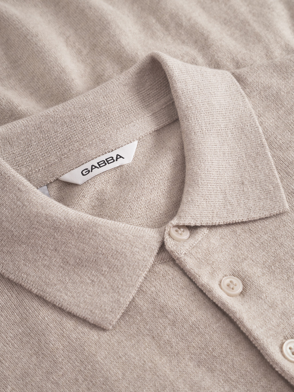 Close-up of the Gabba Akita Prex LS in Sand—a beige long-sleeve knit polo featuring a folded collar, three white buttons, and a “GABBA” label inside the collar, exemplifying refined comfort and premium craftsmanship.