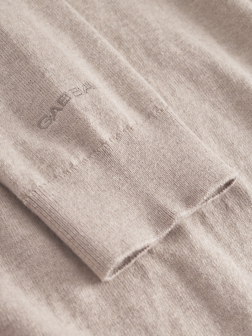 Close-up of the Akita Prex LS - Sand sweater sleeve by Gabba, featuring a subtle ribbed cuff and GABBA embroidery near the wrist. Crafted from premium quality fabric for a soft, smooth texture and refined comfort.
