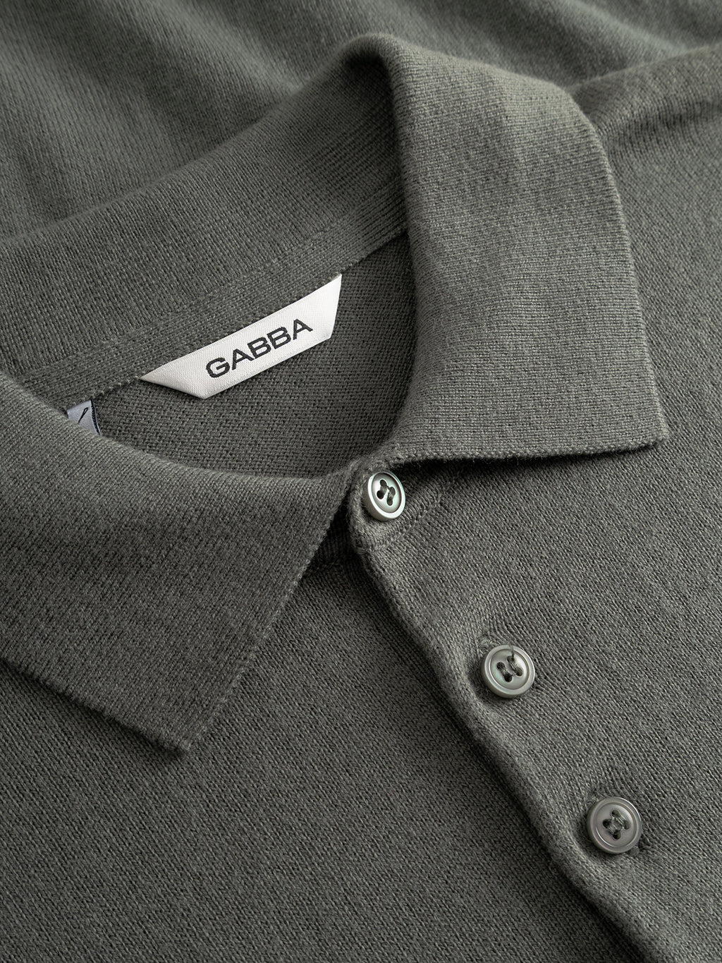 A close-up of the Gabba Akita Prex LS polo in Dust Sage Green, featuring a folded collar, three buttons, and a white Gabba label inside, crafted from soft cotton-cashmere.
