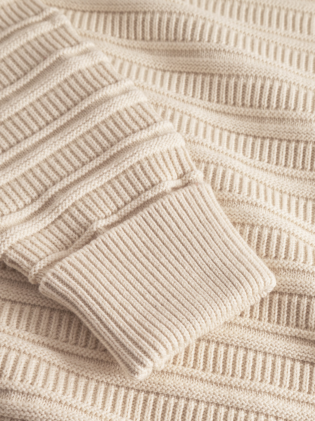 Close-up of the Iwaki Buco LS - White Almond sweater by Gabba, showcasing its soft, cozy beige knit with ribbed cuffs and textured horizontal stripes—a modern take on the classic cotton zip jumper.