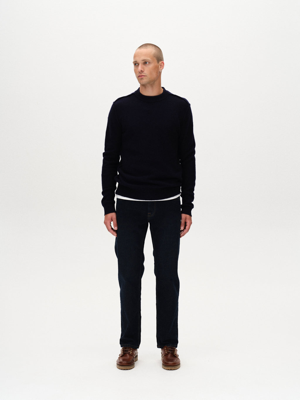 A person stands against a plain white background, wearing a black long-sleeve sweater and Gabbas Marc Jingo - Dark Blue Denim jeans, paired with brown shoes, looking slightly to the side with a neutral expression.