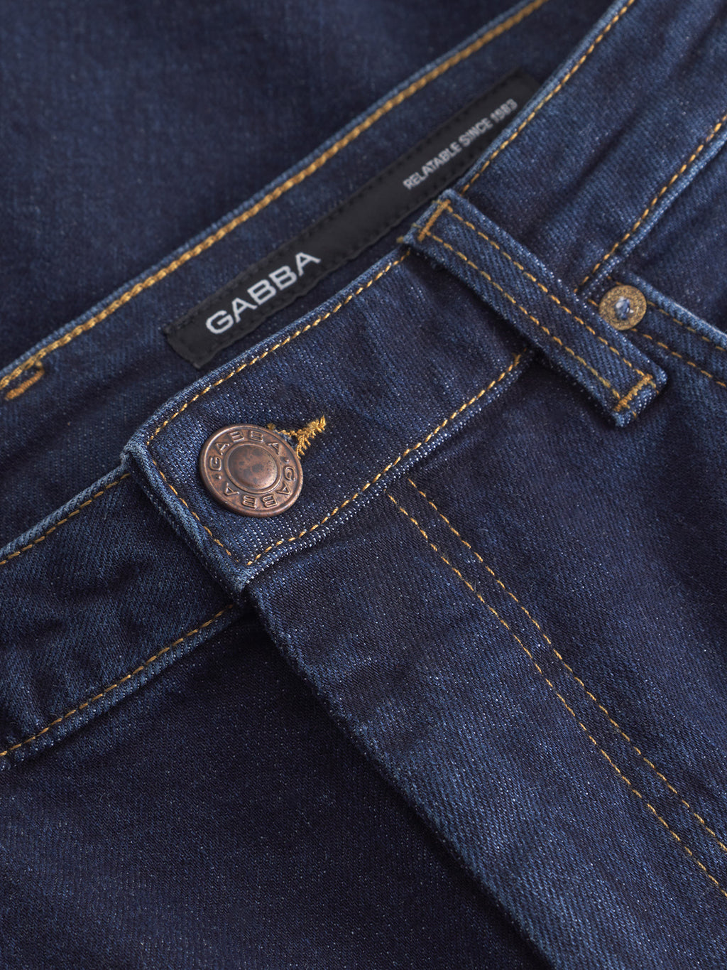 Close-up of the waistband and copper-colored button with engraved text on Gabba Marc Jingo dark blue denim jeans, highlighting the label and belt loop. These dark rinse jeans provide a sleek look and added comfort stretch.