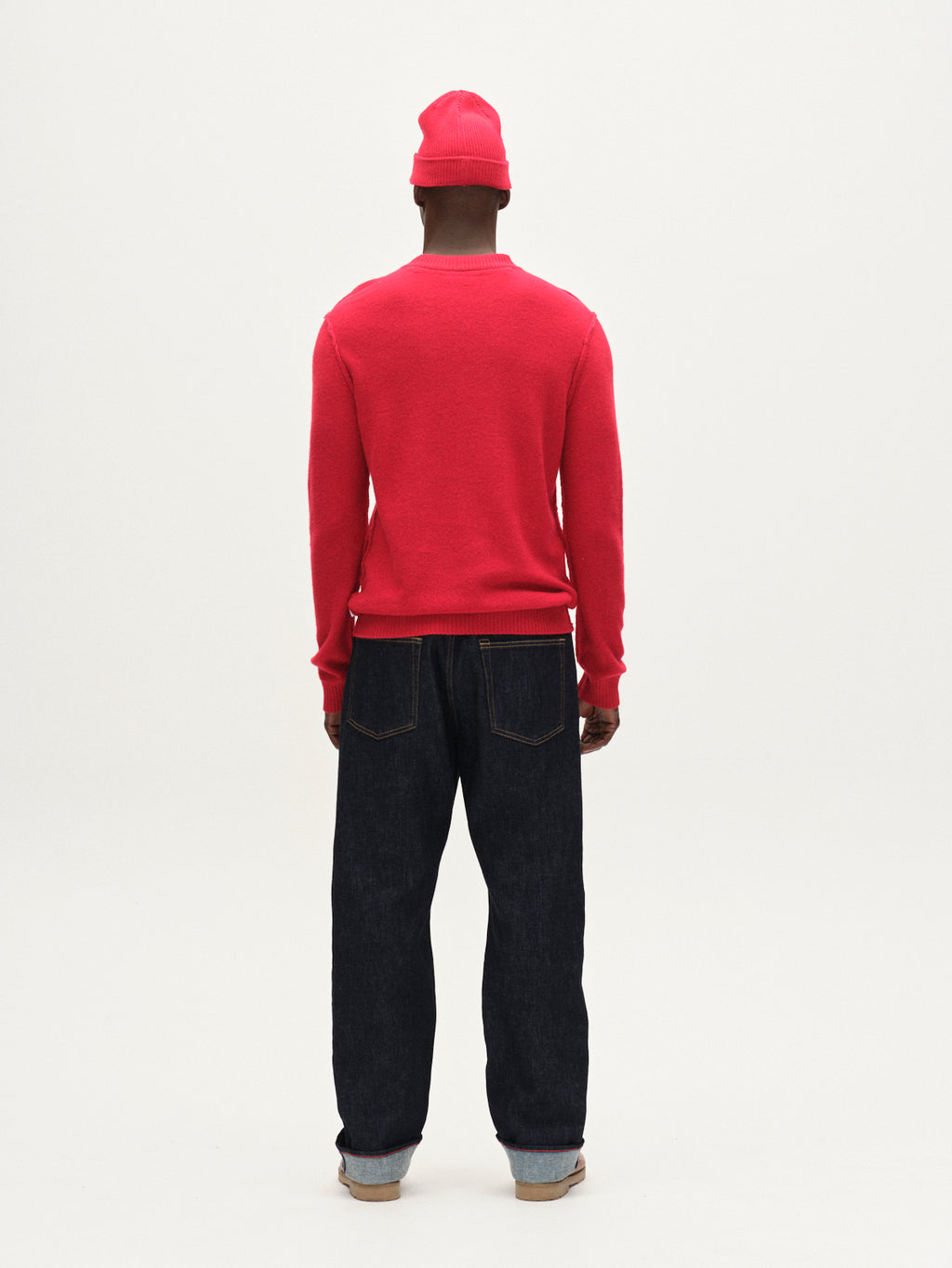 A person faces away from the camera, wearing the Gabba Tokota Aico LS sweater in red with dark blue jeans and rolled cuffs, set against a plain white background.