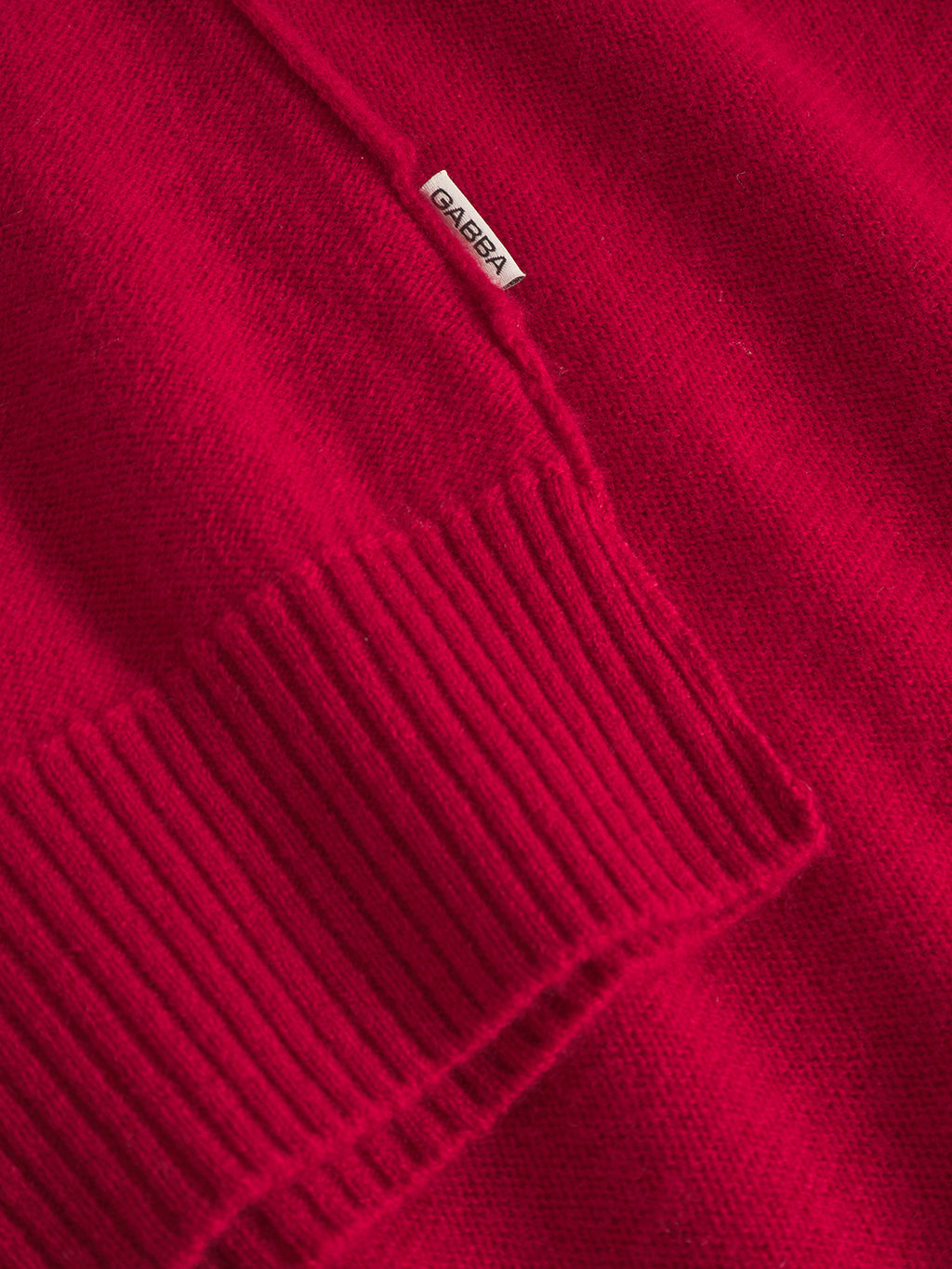 Close-up of the Tokota Aico LS - Red sweater by Gabba, featuring a ribbed cuff and a small white Gabba tag sewn onto the modern red knit fabric.