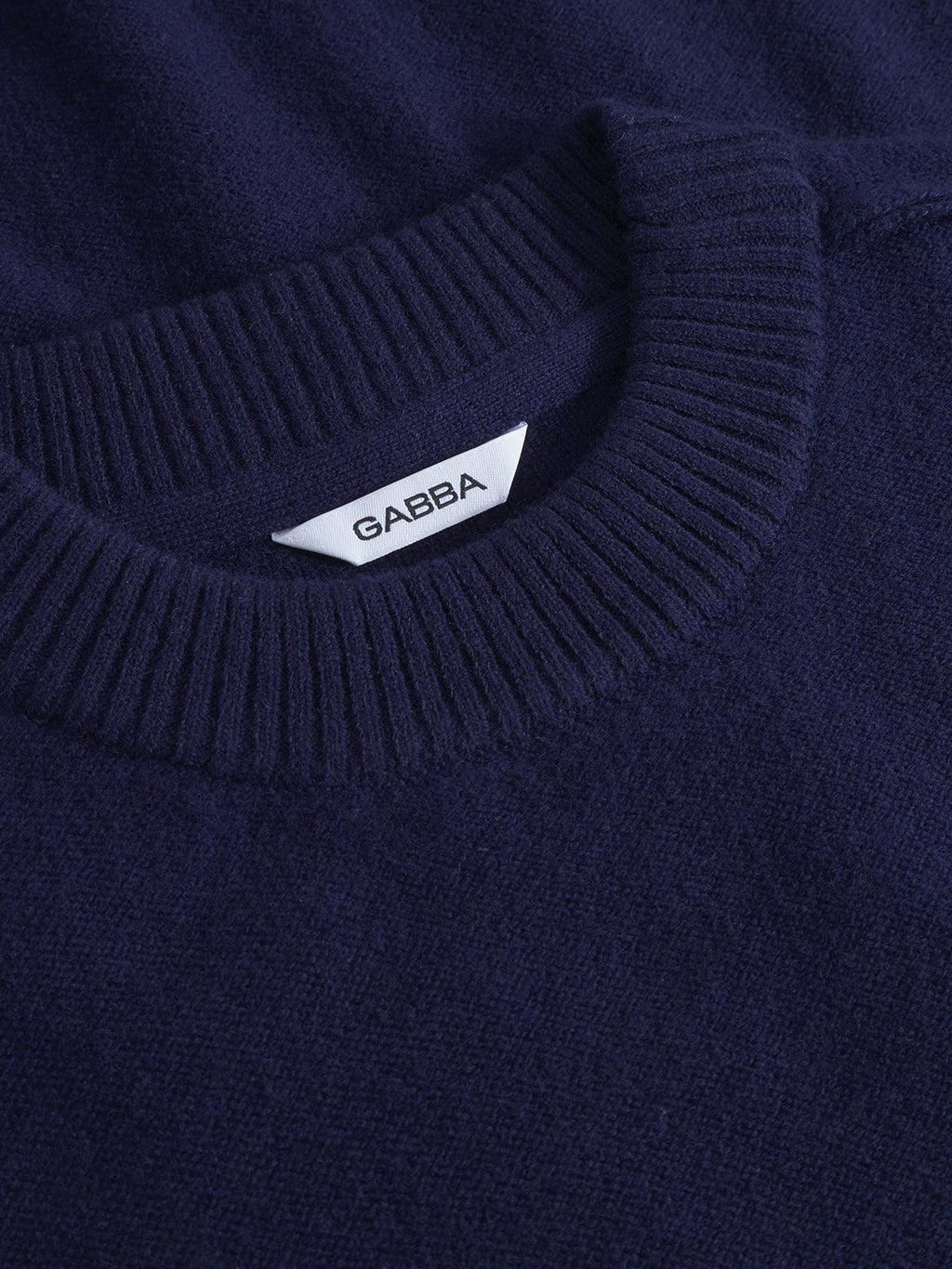 Close-up of the Tokota Aico LS sweater in dark navy, featuring a ribbed crew neckline and a white Gabba label inside the collar—a versatile merino knit layer for any wardrobe.