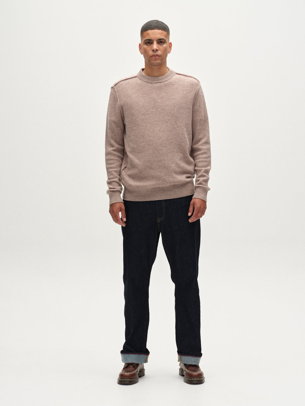 A man stands facing forward against a white background, wearing the Gabba Tokota Aico LS sweater in light brown, paired with dark jeans and brown shoes. His arms rest at his sides and he has a neutral expression.