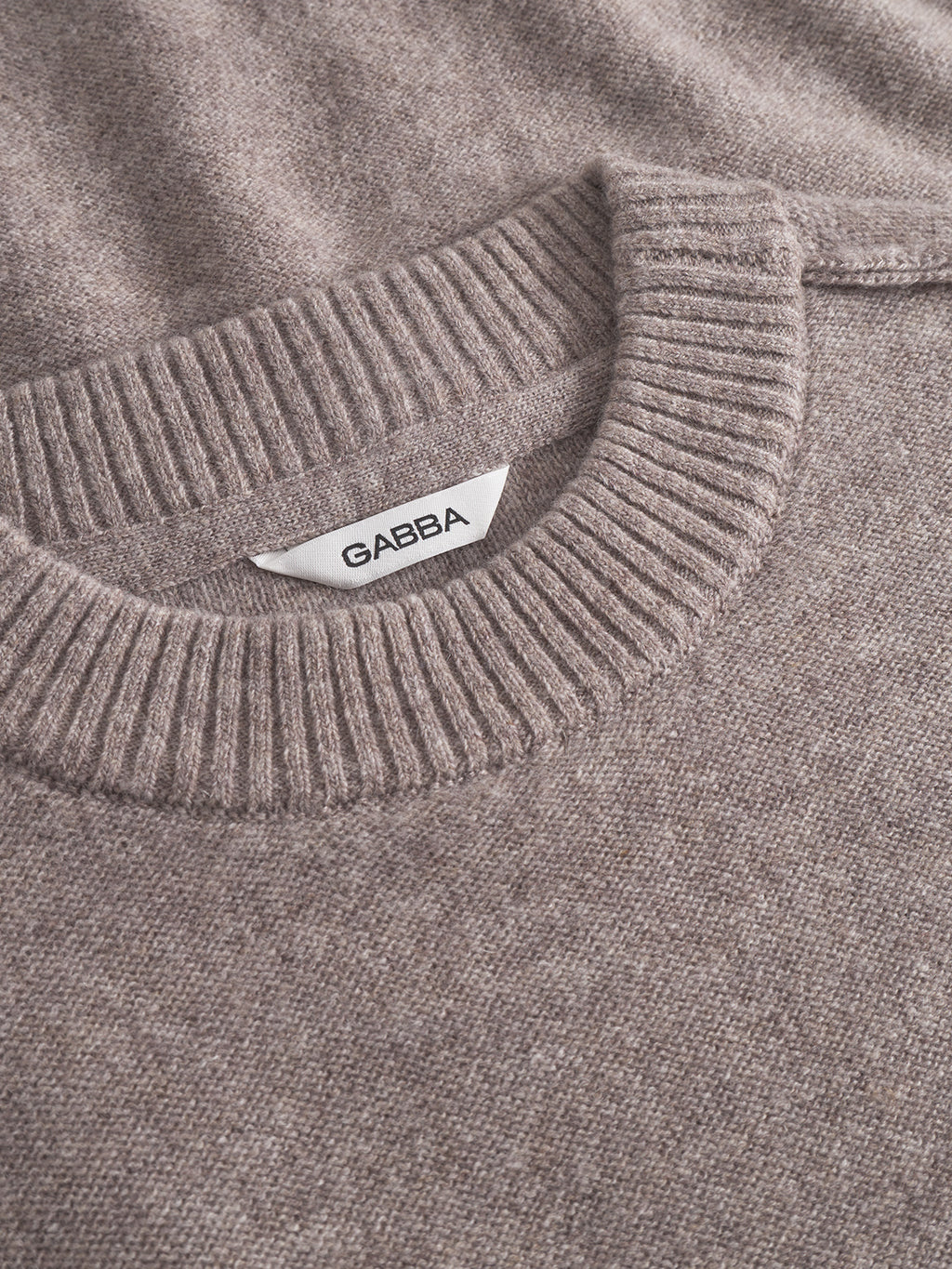 Close-up of the Tokota Aico LS sweater in light brown by Gabba, featuring a structured knit and ribbed crew neck collar, with a white Gabba label sewn inside the neckline.
