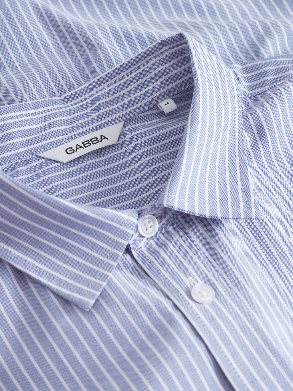A close-up of the Gabba Sven Reg Crest LS shirt in blue stripe, featuring vertical light blue and white stripes, a pointed collar, long sleeves, and a “GABBA” label inside the collar.