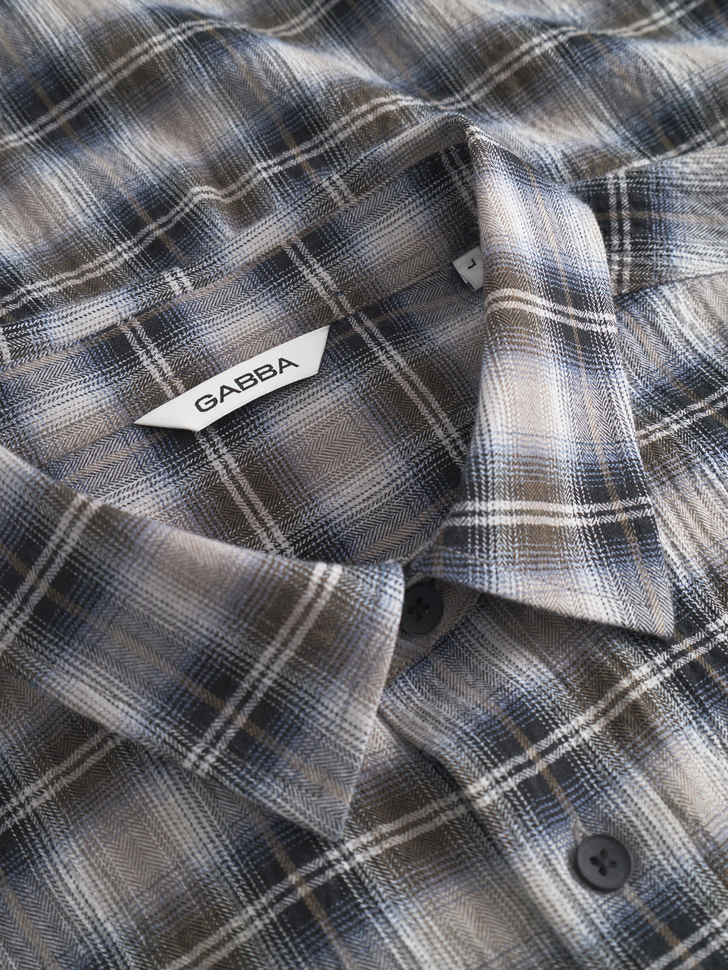 Close-up of the Gabba Sven Reg Crepe LS shirt in blue check, showcasing a collar, dark buttons, and a white label inside the collar with the Gabba brand name—a smart casual long-sleeve option.