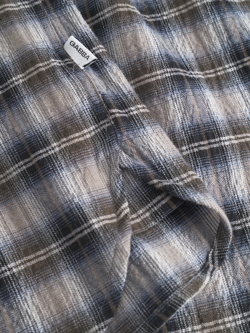 A close-up of the Gabba Sven Reg Crepe LS - Blue Check shirt in brown, blue, and white plaid, with a small white Gabba label near the seam—perfect for smart casual outfits.