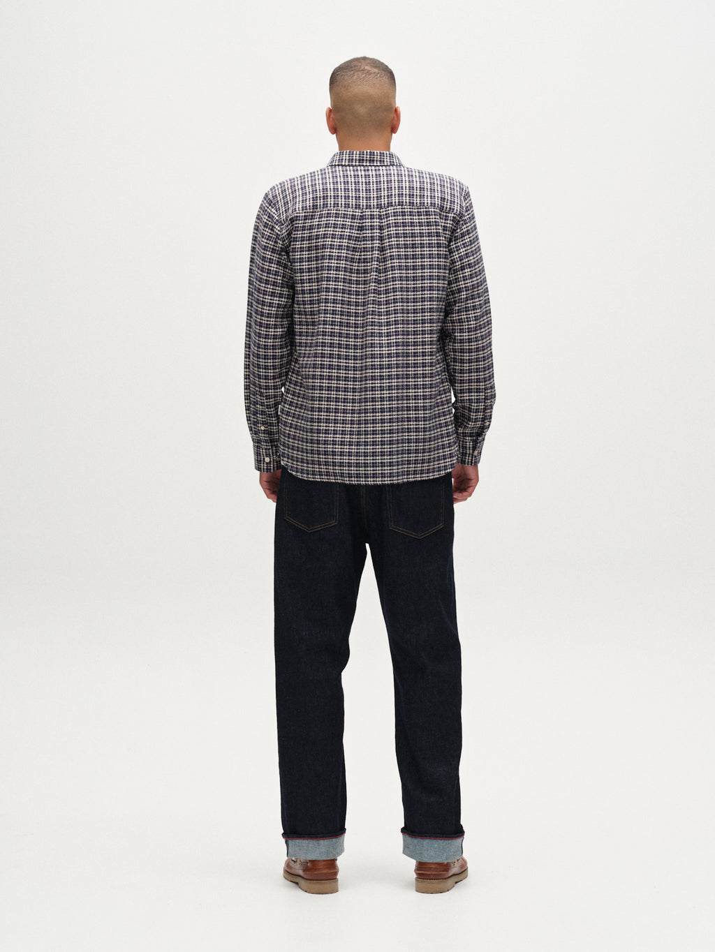 A person faces away from the camera, wearing the Gabba Sven reg TX LS - Blue Check shirt with dark jeans and brown shoes, set against a plain white background.