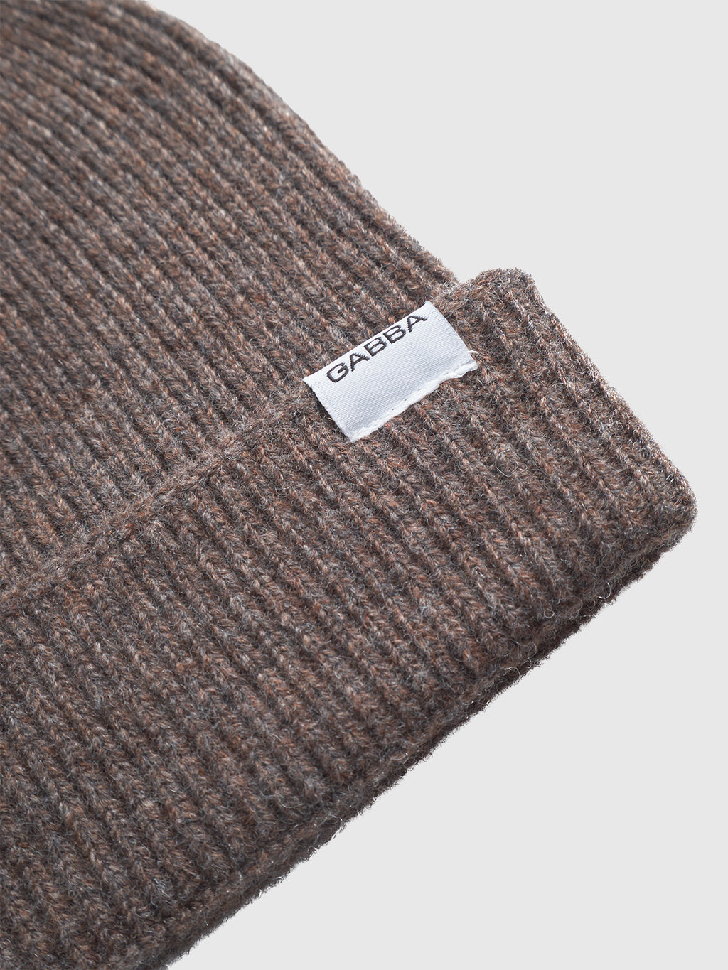 Close-up of the Biella Aico - Dk. Brown beanie by Gabba, crafted from 100% merino wool with a ribbed design, folded brim, and white GABBA tag. Set against a plain, light background—ideal for cold-weather looks.