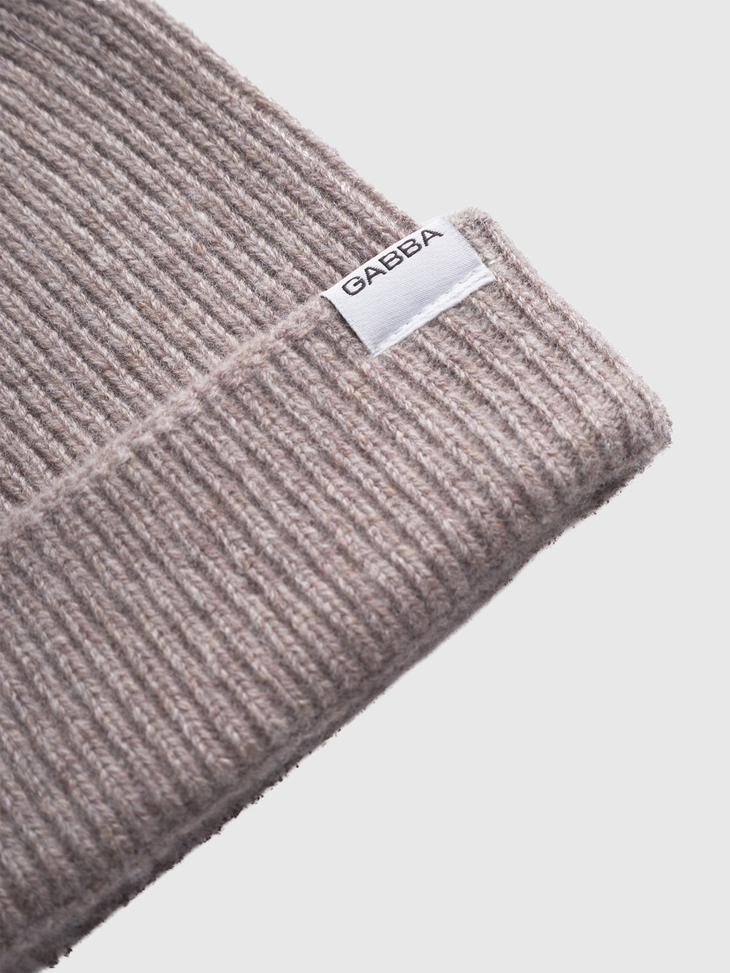 Close-up of the Biella Aico - Lt. Brown ribbed knit wool beanie by Gabba, featuring a white fabric label with the brand name on the folded edge, perfect for winter accessories against a plain light background.