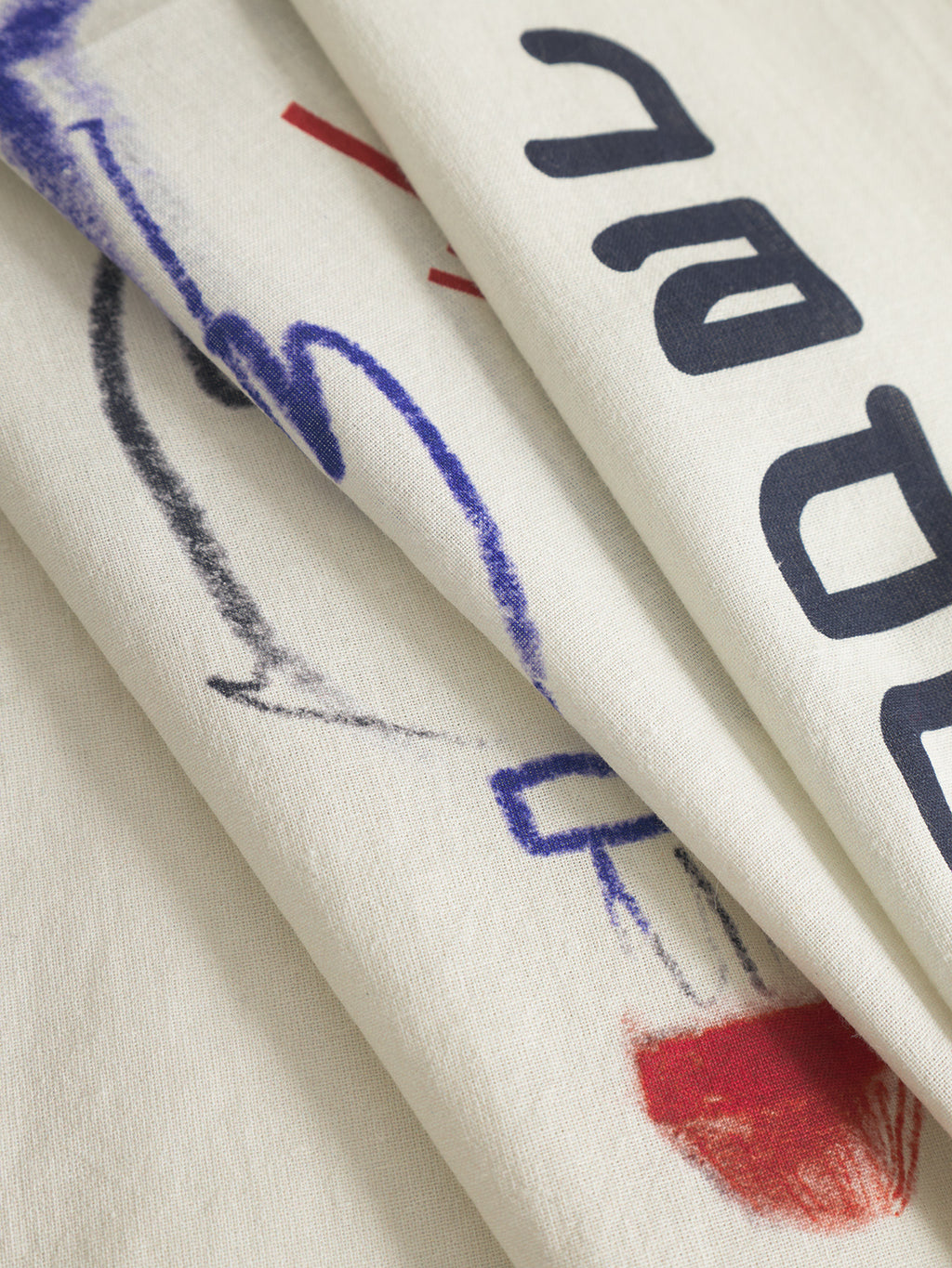 Close-up of Gabbas Bandana Kay - Multi Pattern, showing overlapping off-white fabric with black printed letters, blue and red sketch-style markings, and visible folds that add texture and shadows.