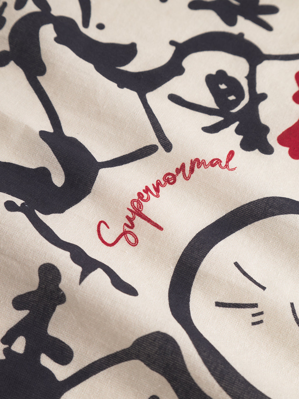 A close-up of Gabbas Bandana Yovi - Multi Pattern shows premium cotton with abstract black line art and Supernormal in red cursive at the center, inspired by Japanese prints on a light off-white background.