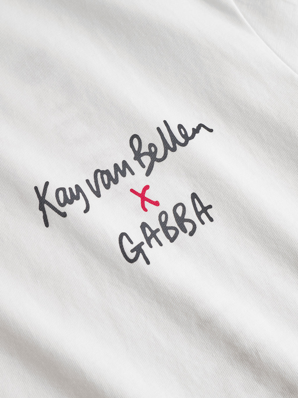 Close-up of the white Gabba Dune Kay Man SS GOTS tee, featuring handwritten-style “Kay van Bellen x GABBA” text in black with a red x, highlighting its sustainable, GOTS-certified design.