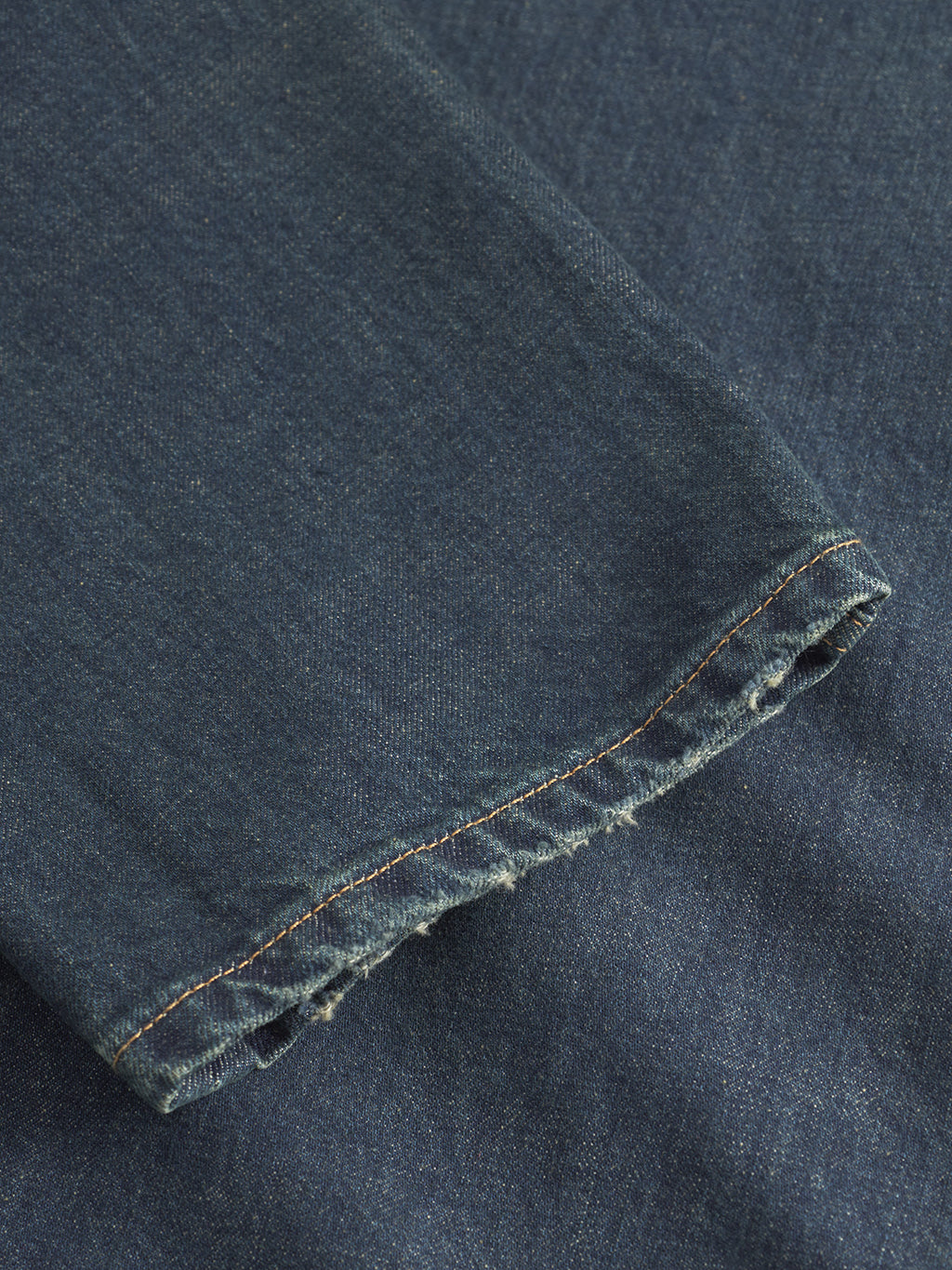 A close-up of the frayed hem and visible stitching on Gabbas Marc Dox dark blue denim straight leg jeans, laid over another denim fabric in a vintage workwear style.