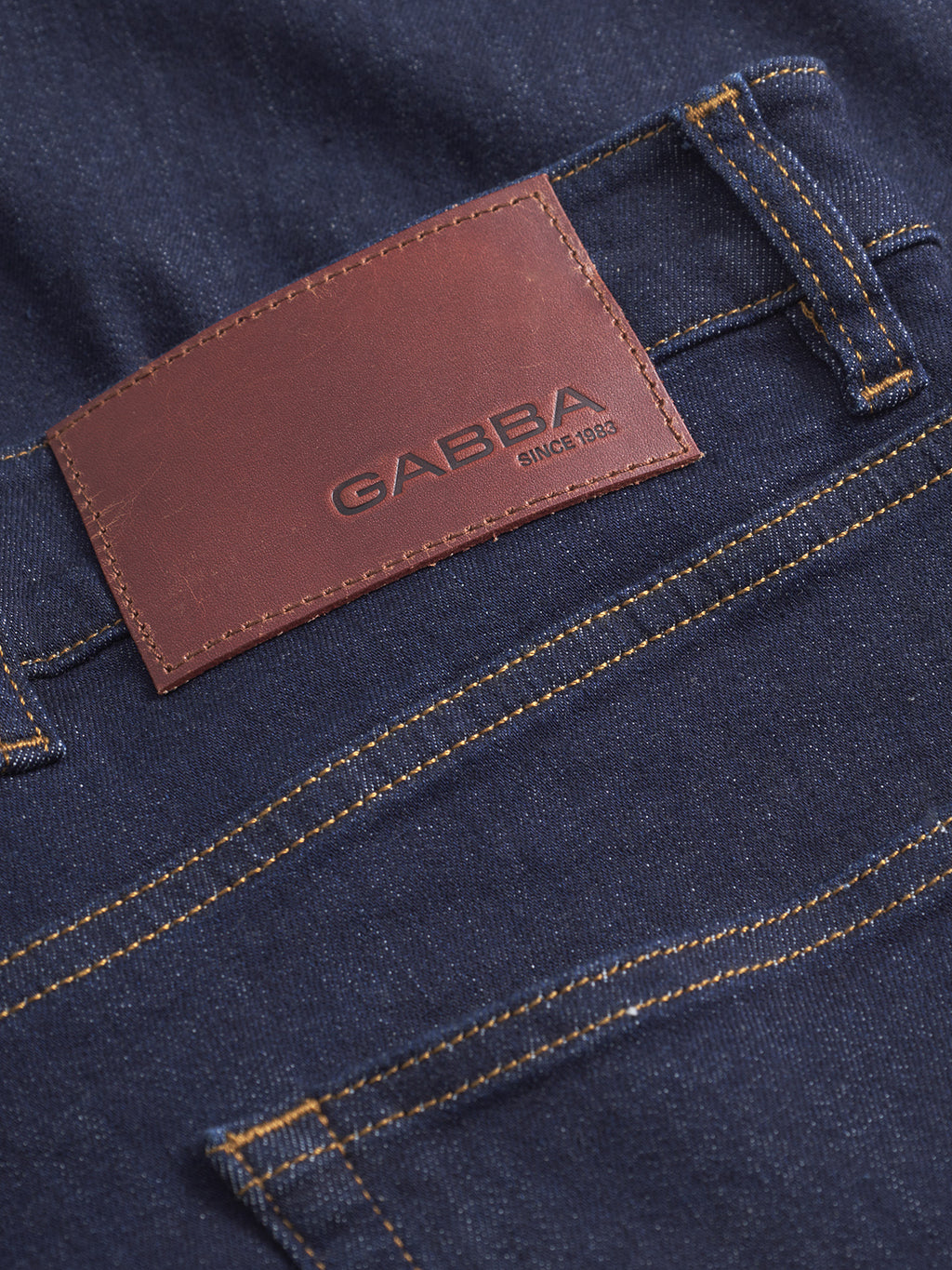 Close-up of the back pocket of Gabba Alex Just - Denim Blue jeans, showing a brown leather patch embossed with the brand name and yellow stitching along the pocket seams.