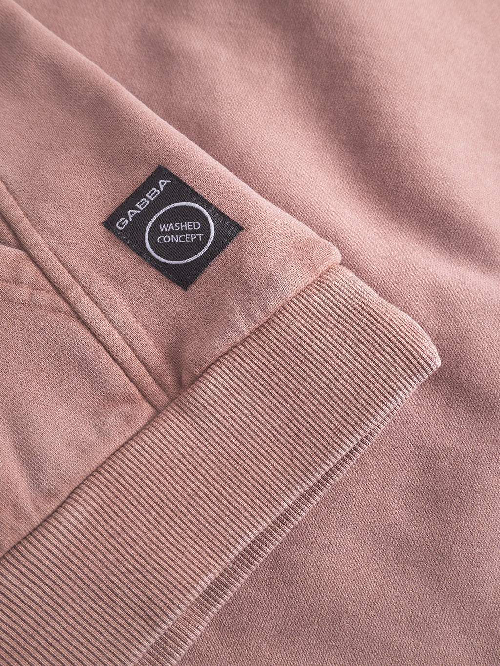 Close-up of the Delphi Bump GWC - Rose sweatshirt by Gabba, showcasing its black label and WASHED CONCEPT tag. The ribbed cuff, texture, and stitching give it a modern casual appeal.