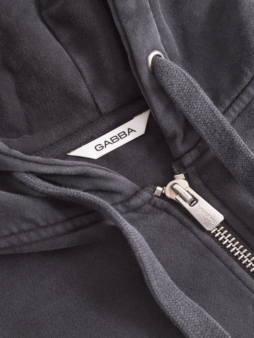 Close-up of the Delphi Bump GWC - Black zip hoodie by Gabba, featuring a metal zipper, drawstrings, and ultra-soft fabric. A white collar label displays the Gabba brand name, emphasizing quality and comfort.