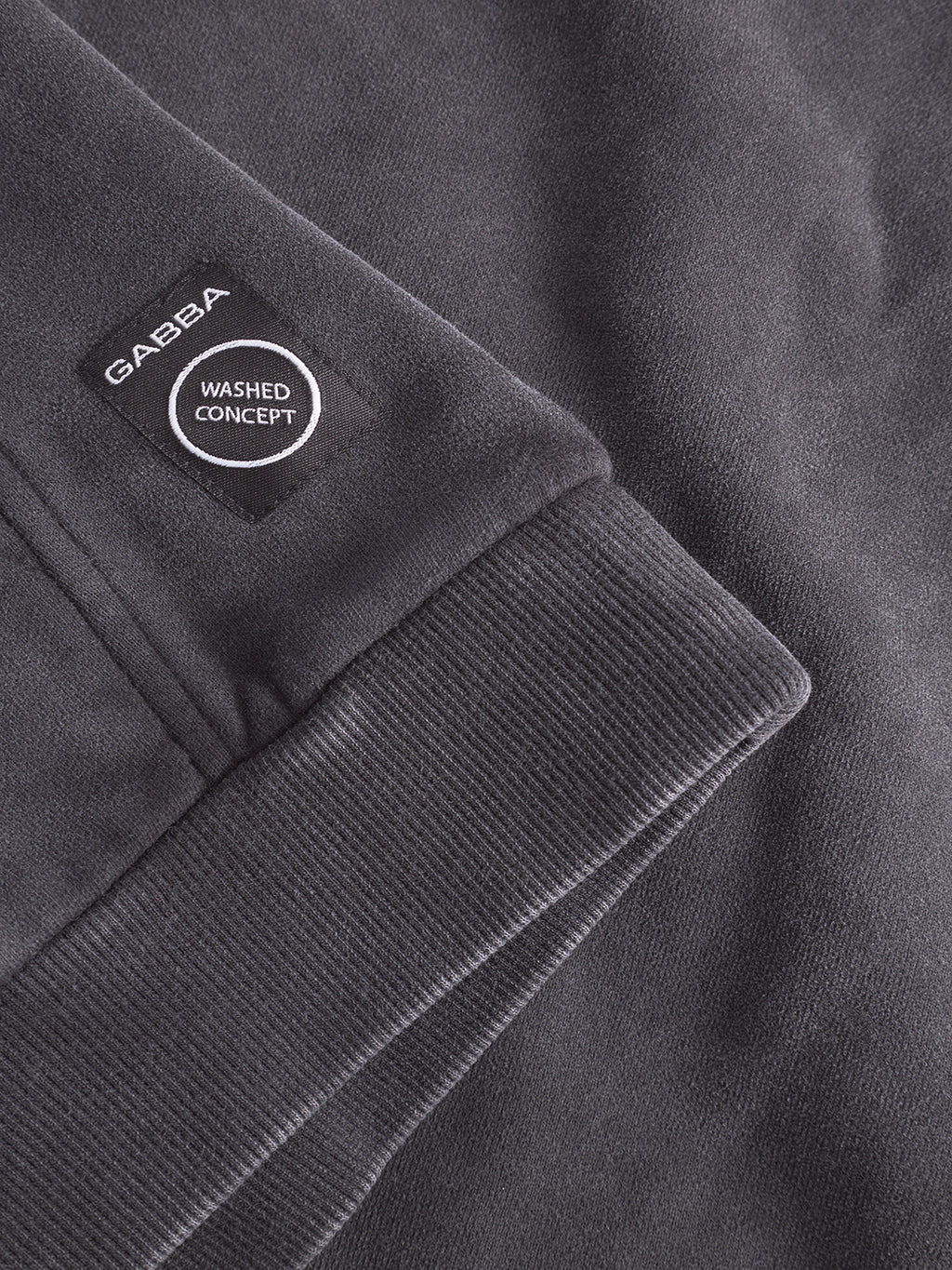 Close-up of the Delphi Bump GWC - Black hoodie sleeve by Gabba, showcasing a black patch with Gabba and Washed Concept in white text. The ultra-soft fabric and ribbed cuff details highlight its cozy style.