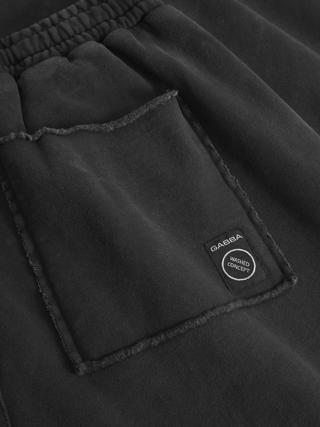 Close-up of Gabba Pireo Bump GWC pants in black, featuring a straight fit, elastic waistband, raw-edged patch pocket, and a small black label with Gabba and Washed Concept text.