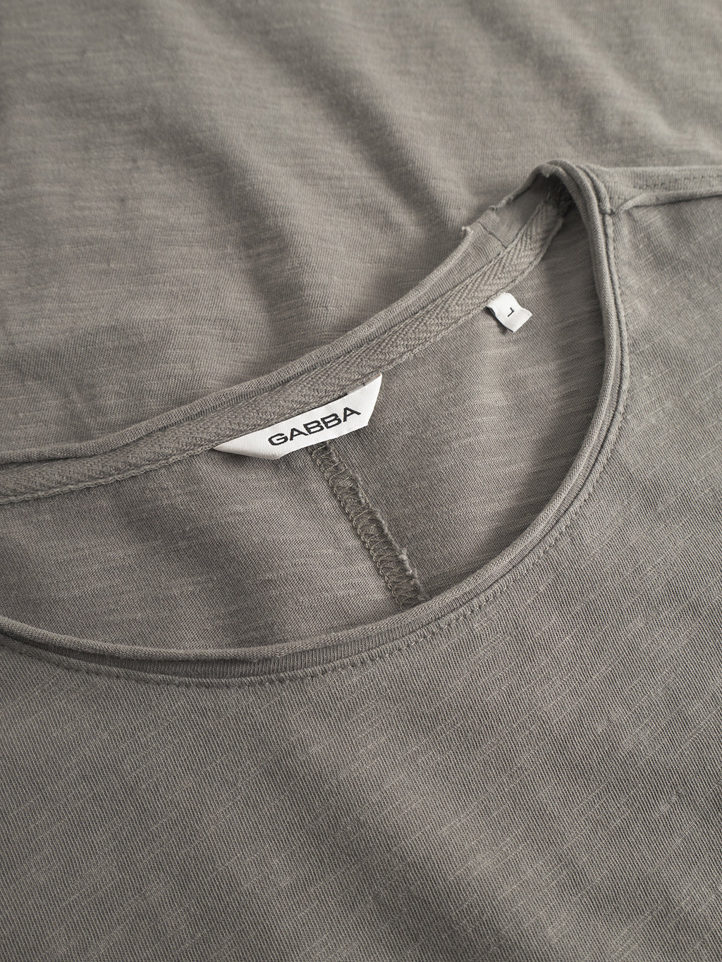 Close-up of the Gabba Paros Rif GWC - Grey long sleeve tee with a round neckline and visible white Gabba label. The image highlights its super soft cotton, faded look, and detailed stitching.